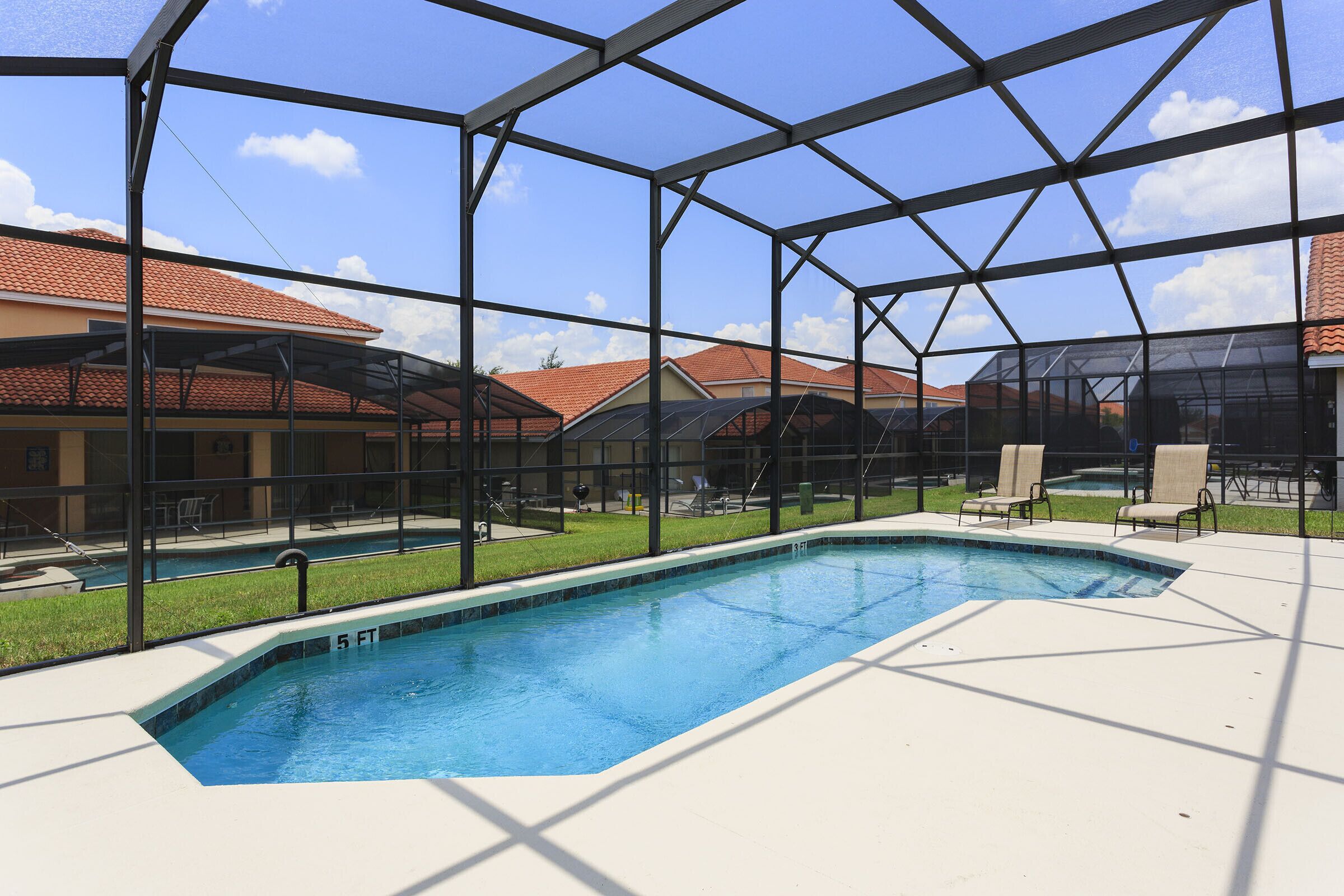 A swimming pool with a glass enclosure, surrounded by lounge chairs and a covered patio area.