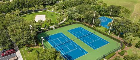 An aerial view of a tennis court complex surrounded by lush greenery and residential buildings.