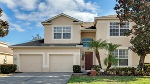 A two-story house with a garage, a red door, and a small garden with palm trees.