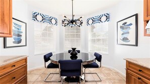 A dining area with a round table, blue upholstered chairs, and a black chandelier.