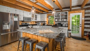 A kitchen with a large island, stainless steel appliances, wooden beams, and bar stools.