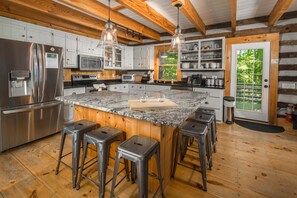 A kitchen with a large island, stainless steel appliances, wooden beams, and bar stools.