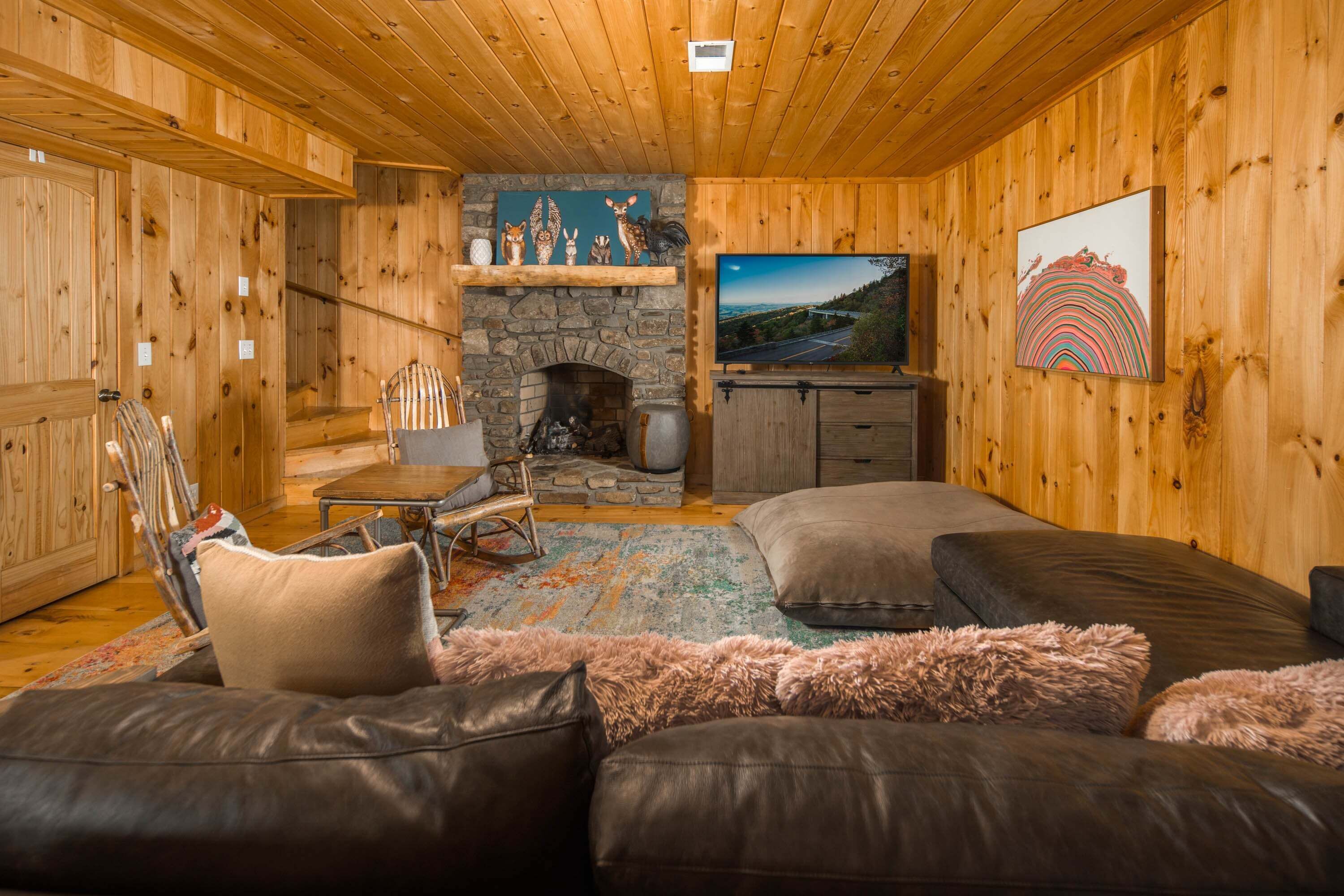 A cozy cabin interior with a stone fireplace, wooden walls, a television, and a plush sofa.