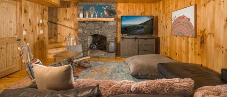 A cozy cabin interior with a stone fireplace, wooden walls, a television, and a plush sofa.