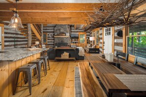 A rustic log cabin interior with a kitchen, dining area, and seating.