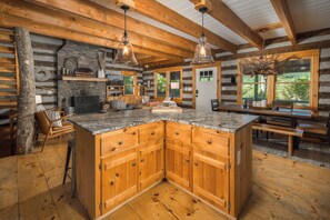 A log cabin interior with a central island kitchen, wooden cabinets, and a stone fireplace.
