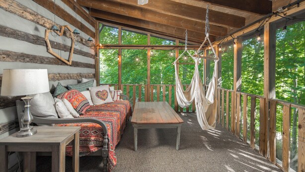 A rustic wooden cabin with a bed, a table, and a hammock.
