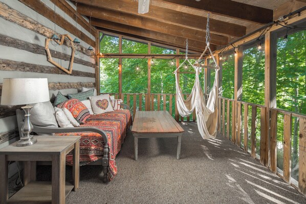 A rustic wooden cabin with a bed, a table, and a hammock.
