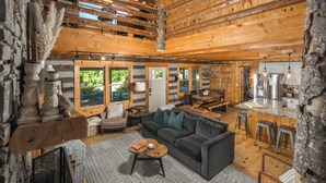 A log cabin interior with a living area, kitchen, and large windows.