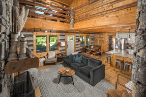 Interior de una cabaña de troncos con sala de estar, cocina y ventanas amplias.