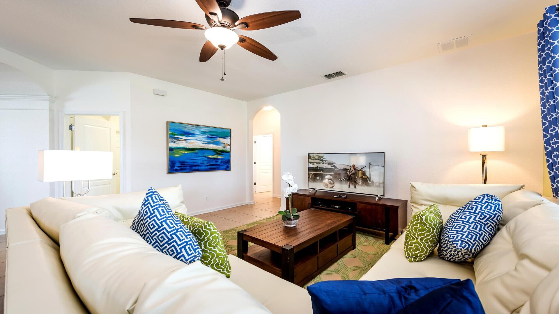 A living room with a ceiling fan, a TV, a coffee table, and two sofas with patterned cushions.