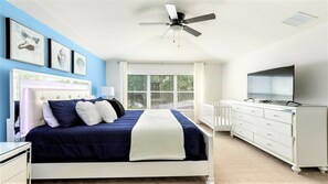 Une chambre à coucher comprenant un lit, un ventilateur de plafond, une commode, un téléviseur et une fenêtre avec des stores.