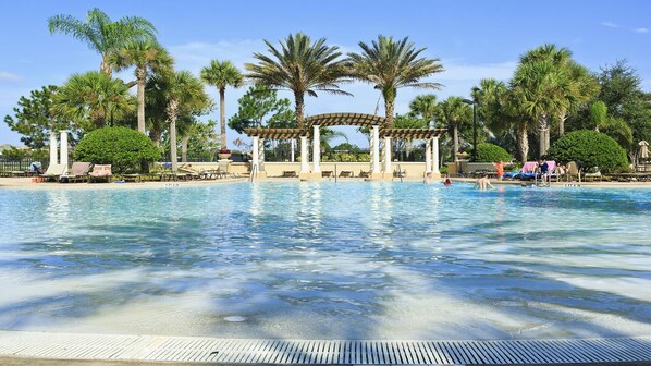 Relax by the serene pool surrounded by lush palm trees and a shaded pergola.