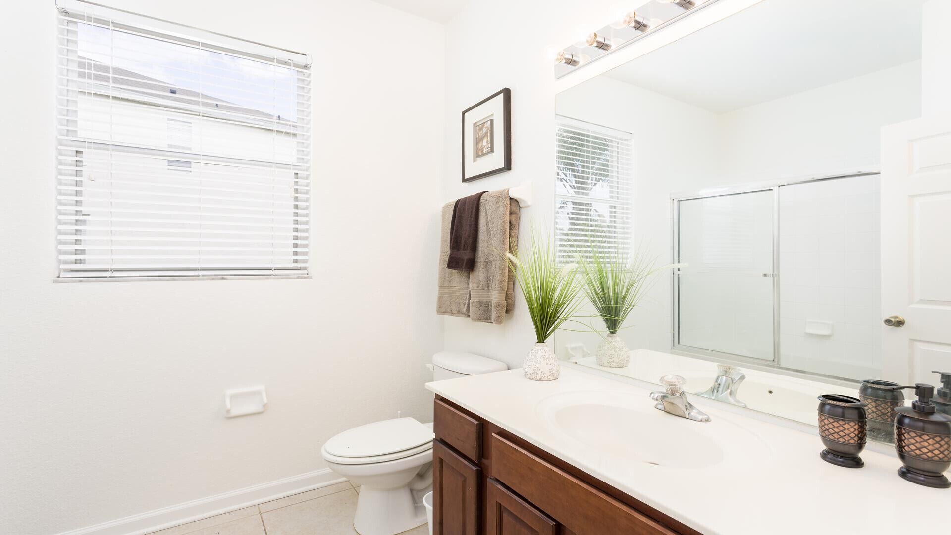 A modern bathroom with a toilet, sink, and large mirror. There are towels hanging on the wall and a plant on the sink counter.