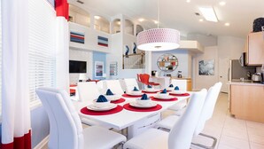 Un comedor moderno con una mesa blanca dispuesta para seis personas, individuales rojos y sillas blancas.