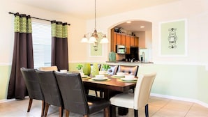 Un comedor con una mesa dispuesta para cuatro, una cocina al fondo y un elemento decorativo en la pared.