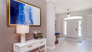 Un couloir avec une console blanche, un banc bleu et un grand tableau abstrait.