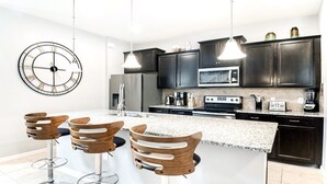 Una cocina moderna con armarios oscuros, una isla grande con taburetes de bar, un reloj y varios electrodomésticos.