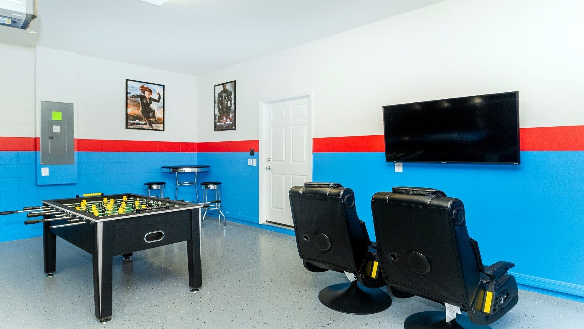 A room with a foosball table, two bar stools, a television mounted on the wall, and a door.