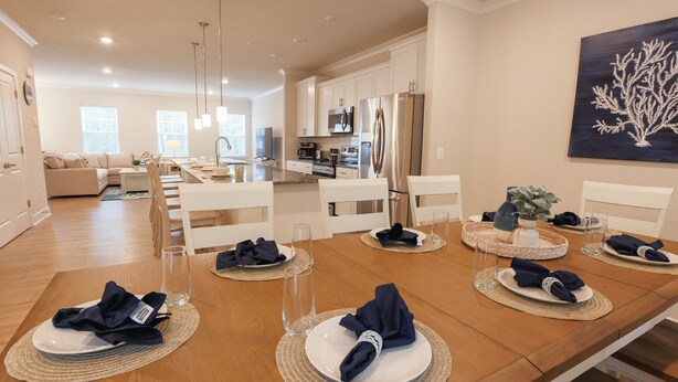 Uma sala de jantar com uma mesa de madeira posta para seis pessoas, cercada por cadeiras brancas.