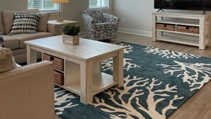 Sala de estar com sofá, poltrona, mesa de centro, rack para TV e tapete estampado.