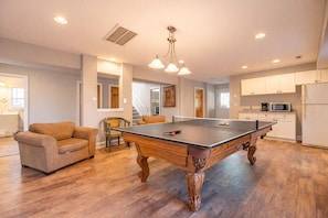 Uma sala ampla com mesa de bilhar, sofá e mesa de jantar.