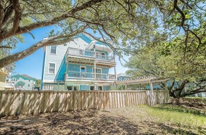 A multi-story building with a balcony, surrounded by trees and a wooden fence. - Allora - Corolla, Ocean Sands, 450 Yds to Beach, Pool, Hot Tub, Pool Table, Gas Fireplace, Pets OK (Corolla)