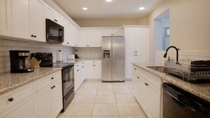 Una cocina con armarios blancos, electrodomésticos de acero inoxidable y suelo de baldosas.