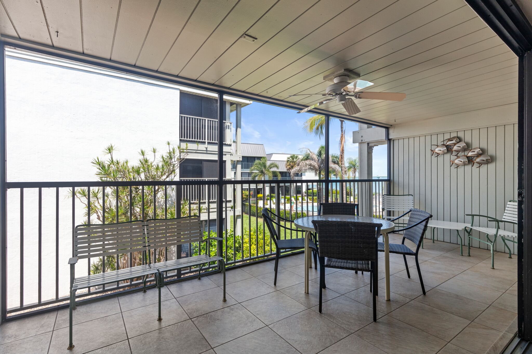 A balcony with a table and chairs, a bench, and a view of a building and greenery.