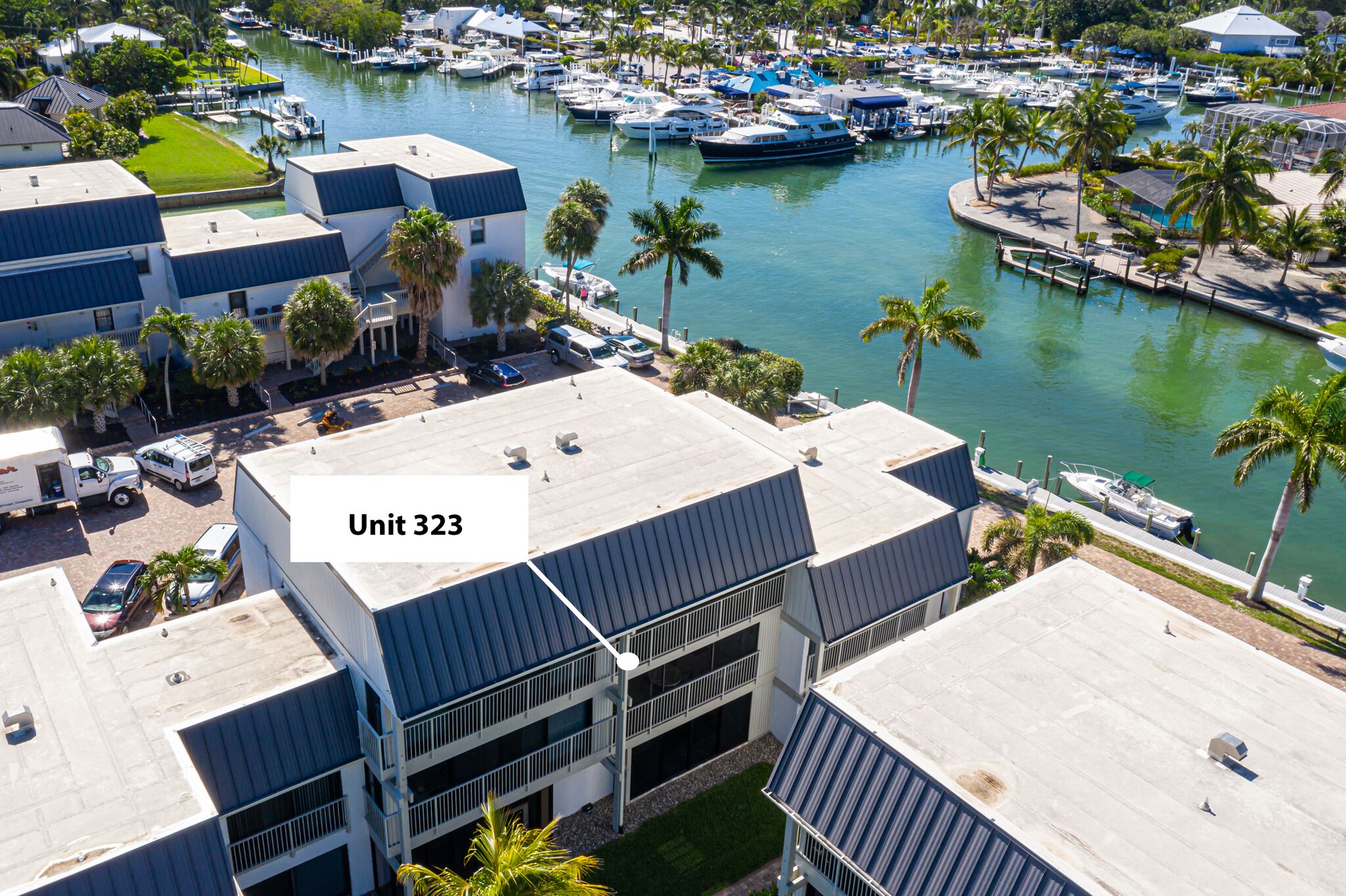Un port de plaisance avec des bateaux, un bâtiment portant l’inscription « Unité 323 », et des palmiers tout autour.