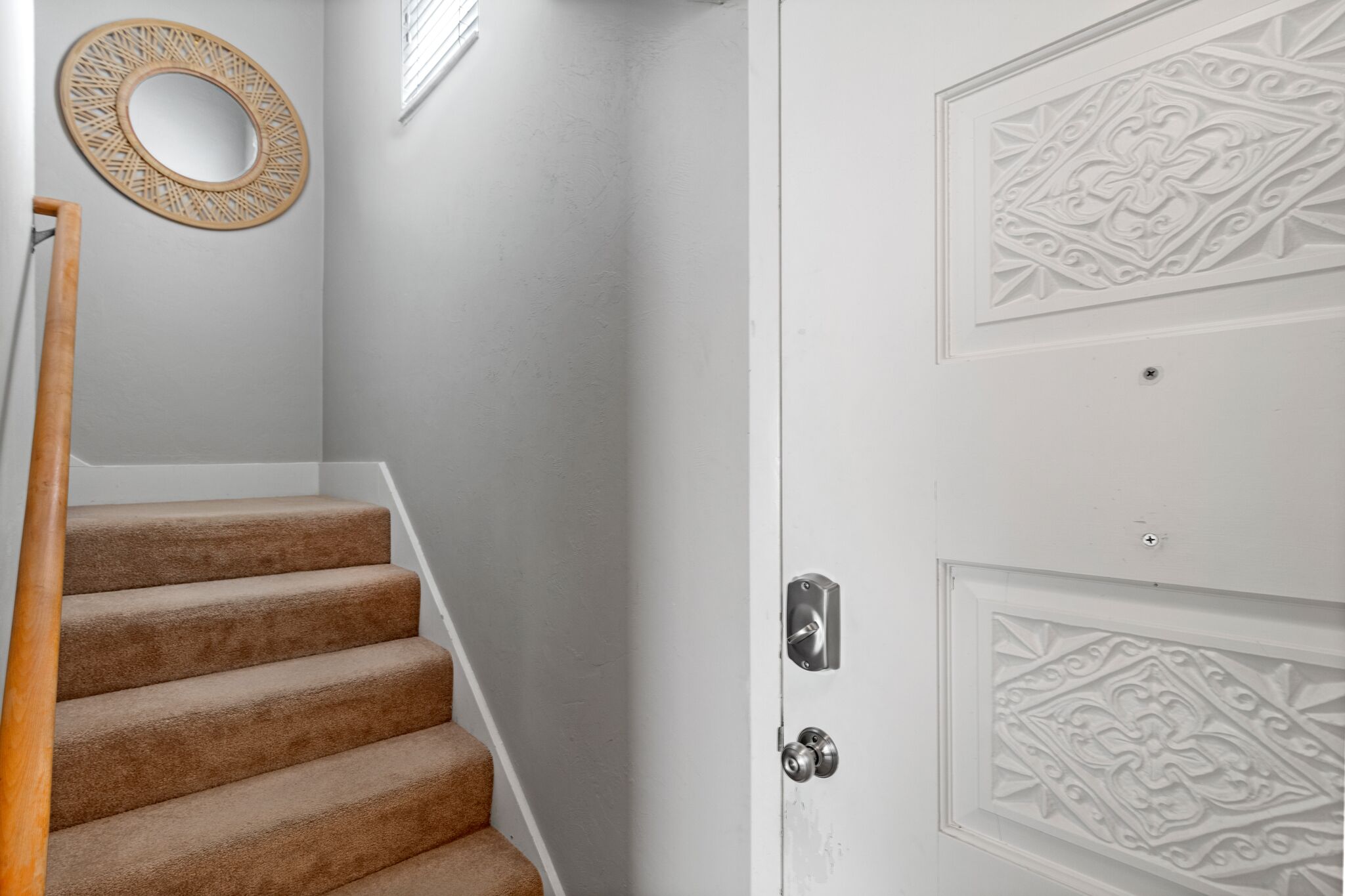 A staircase with carpeted steps leading to a white door with decorative paneling.