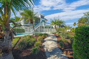 A multi-story house with a pool, surrounded by palm trees and a gravel path.