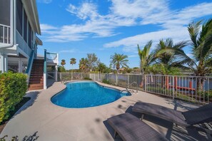 A swimming pool with a white fence, lounge chairs, and a staircase leading to a balcony.