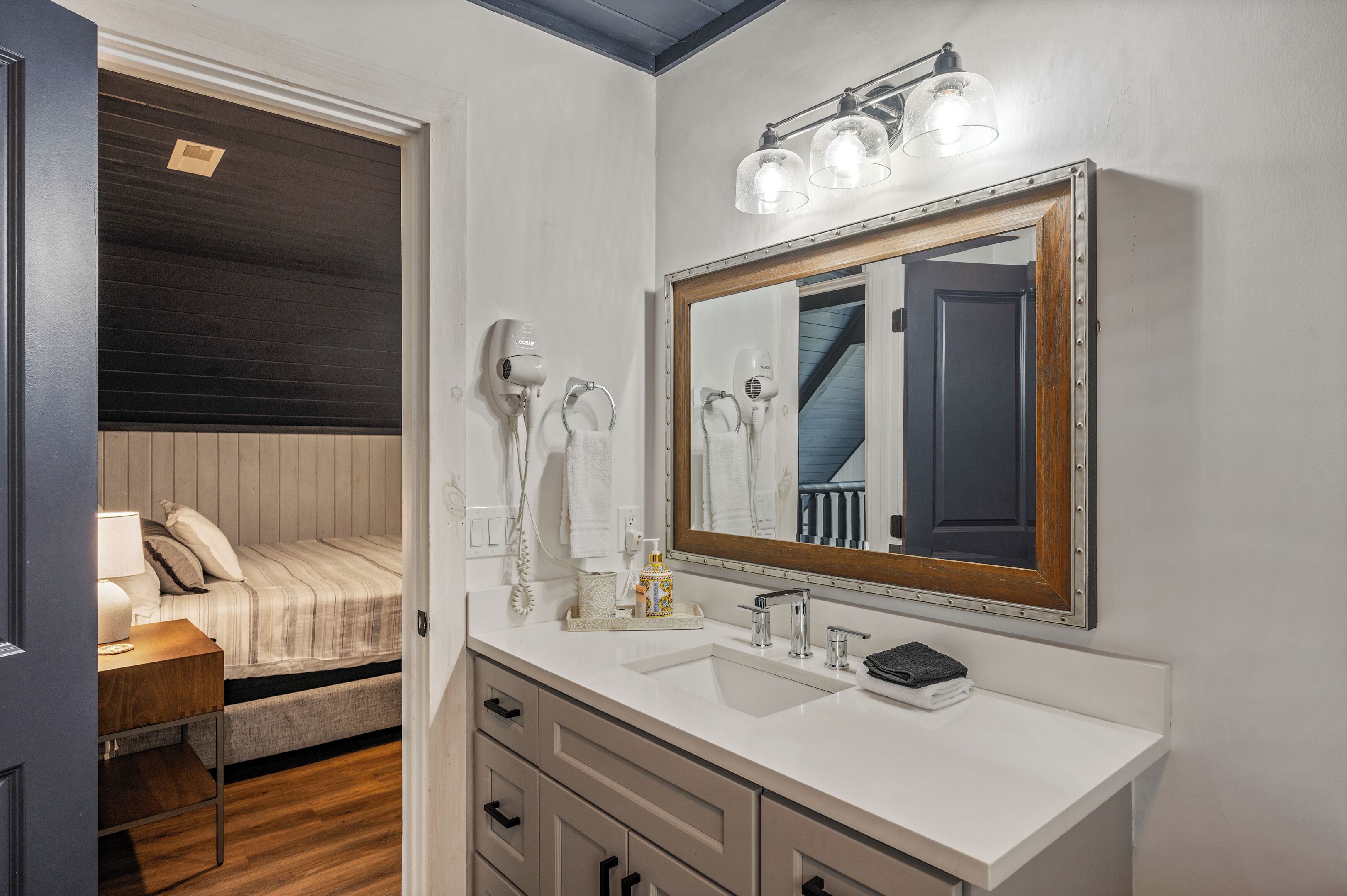 A compact bedroom with a bed, bedside table, and a large mirror with lights.
