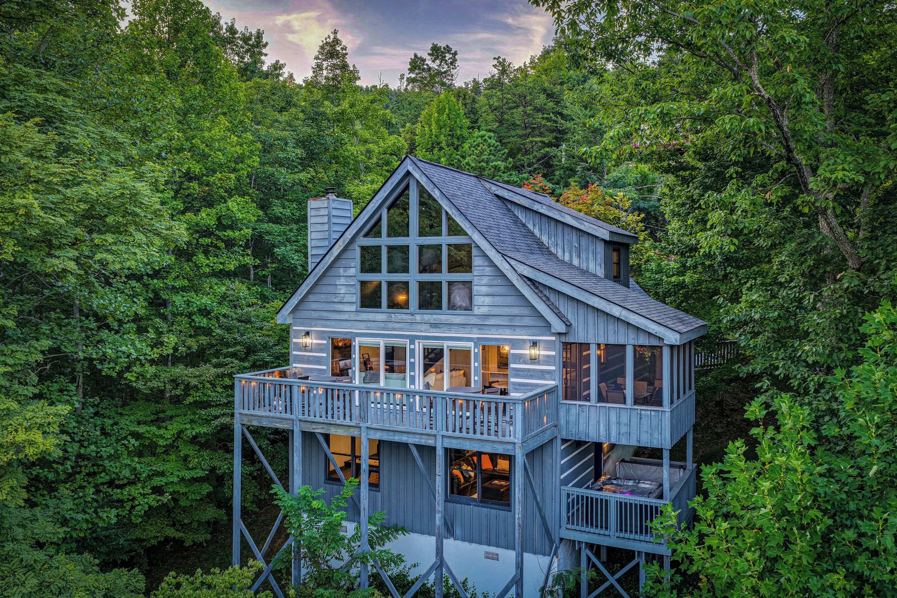 A wooden cabin with a balcony, surrounded by dense forest.