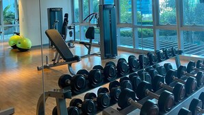 Ett gym med träningsutrustning, stänger för vikter och stora fönster som ger utsikt över omgivningen.