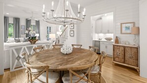 A spacious dining area with a round wooden table, surrounded by wooden chairs, and a large crystal chandelier. - Next to Dragonfly Pool with Designer Interiors, LSV (golf cart), Bikes, and More (Santa Rosa Beach)