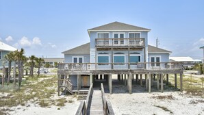 Ein zweistöckiges Strandhaus mit einer Holzterrasse und einer Treppe zum Eingang.