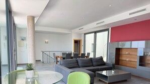 A modern living room with a grey sofa, green chairs, a glass coffee table, and a red accent wall. - Agi Canyelles Mar Casa 1 Casa for rent in Roses Girona. (Roses)