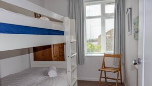 Ein Schlafzimmer mit Etagenbett, Holzstuhl und einem Fenster mit Vorhängen.
