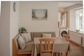 Une pièce confortable avec un canapé, une table à manger, une chaise, une horloge, un tableau, un meuble, un lave-linge et une fenêtre.
