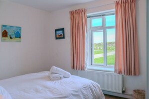 Une chambre à coucher avec un lit, une fenêtre avec des rideaux, un radiateur et deux tableaux accrochés au mur.