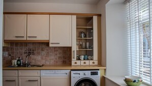 Eine kompakte Küche mit Geschirrspüler, Waschmaschine und einem Fenster mit Jalousien.
