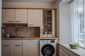 A compact kitchen with a dishwasher, washing machine, and a window with blinds.