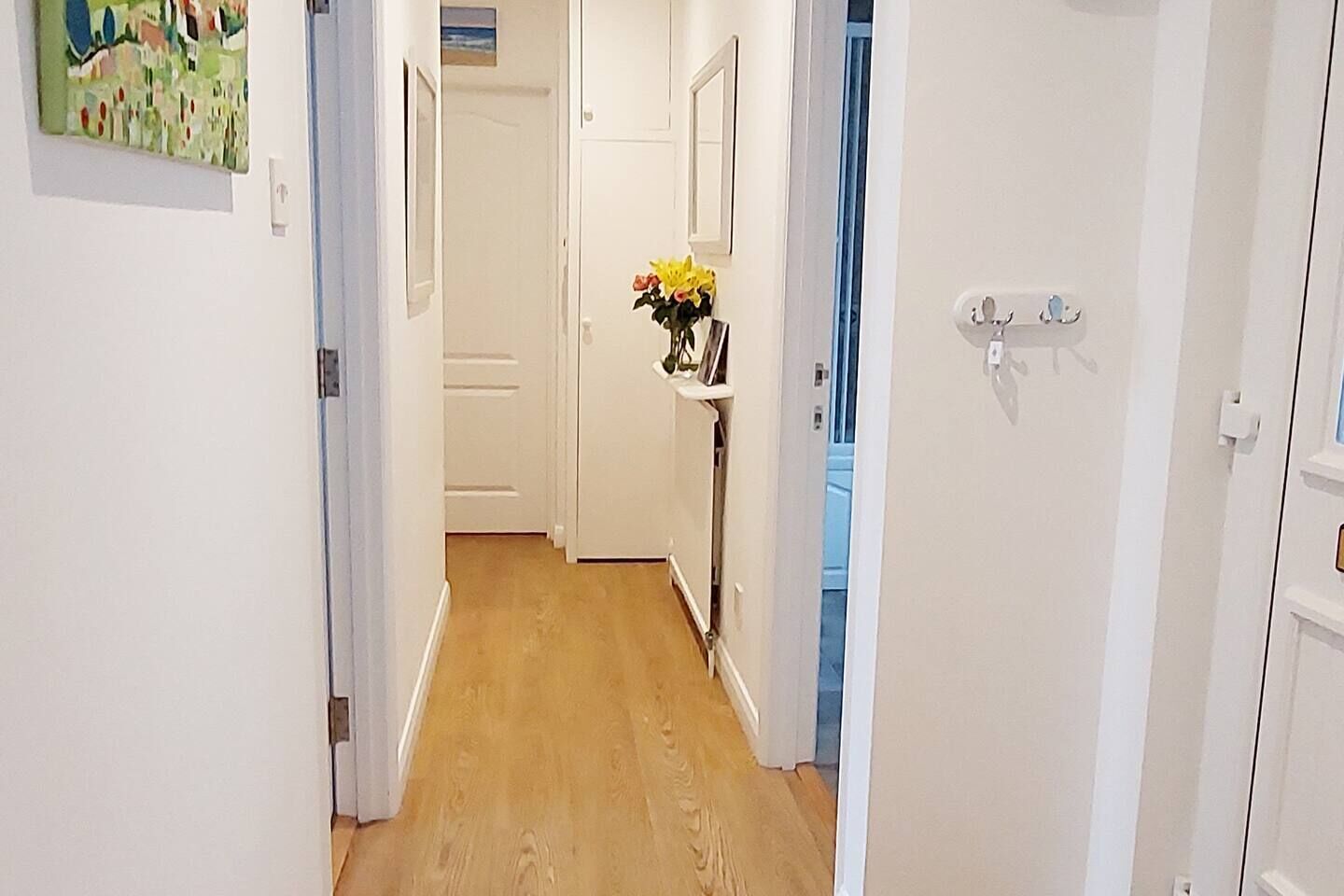 Un couloir aux murs blancs, doté d’un plancher en bois et d’une porte donnant sur une autre pièce.
