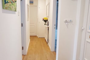 A hallway with white walls, wooden flooring, and a door leading to another room.