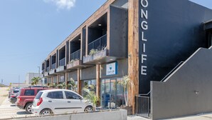 A modern building with a sign reading "LONG LIFE" and a "Clean Life" sign below. There are multiple balconies and a parking area with several cars.