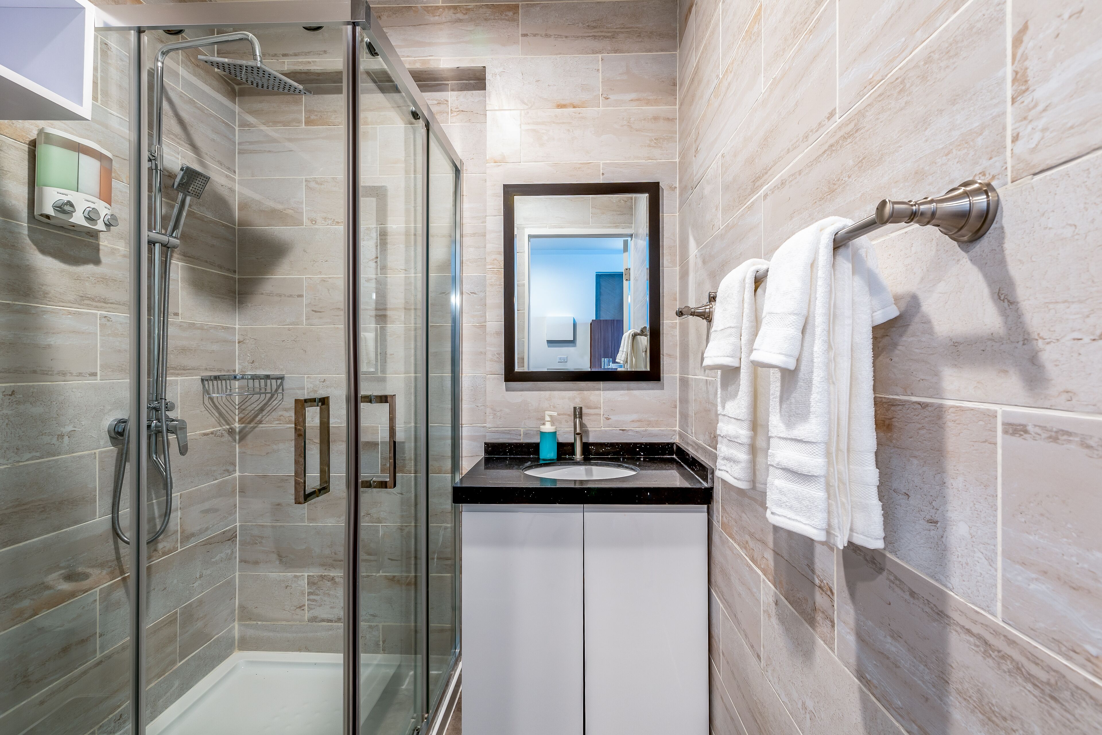 Une salle de bain moderne avec une douche à parois de verre, un lavabo avec un miroir au-dessus et un porte-serviettes fixé au mur.