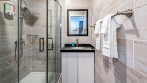 A modern bathroom with a glass-enclosed shower, a sink with a mirror above it, and a towel rack on the wall.