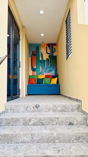 A staircase leading to a room with a colorful wall mural and a blue sofa. - Bushiri's Long Life Building-Studio-Sleeps 2 #10 (Oranjestad-West)